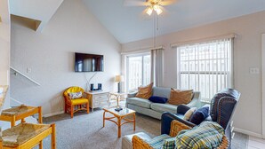 Ein Wohnzimmer mit einer Couch, Sesseln, einem Couchtisch, einem Fernseher und einer Treppe.