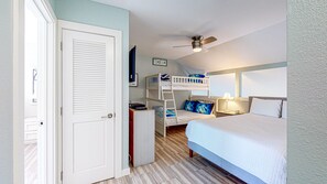 Une chambre avec des lits superposés, un bureau, une chaise, une armoire, un ventilateur de plafond et une table de chevet avec une lampe.