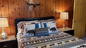 A bed with a patterned bedspread, two bedside lamps, and a wooden wall with a mounted animal head. - Cottage #3 near a Creek & Pond on Mt. Lassen (Shingletown)
