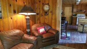 A cozy room with a leather armchair, a lamp, and a wooden wall with a clock. - Cottage #3 near a Creek & Pond on Mt. Lassen (Shingletown)