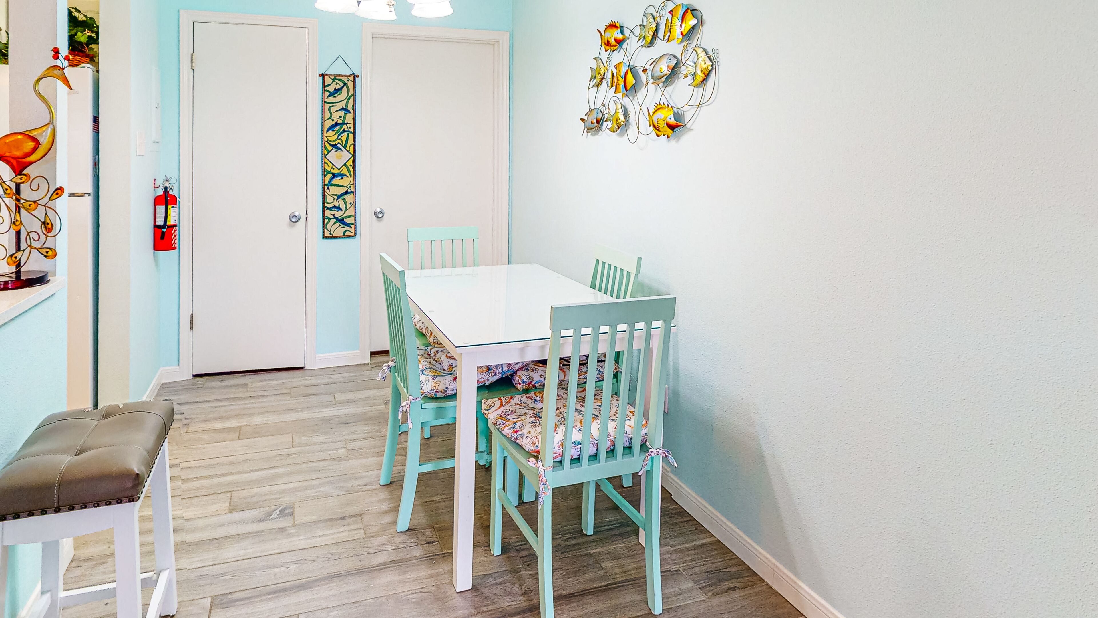 Un'area pranzo con un tavolo bianco e sedie color acquamarina, un pavimento in legno e un elemento decorativo a parete.