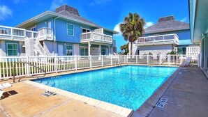Zwembad met een witte omheining, een palmboom en een gebouw met twee verdiepingen en balkons.