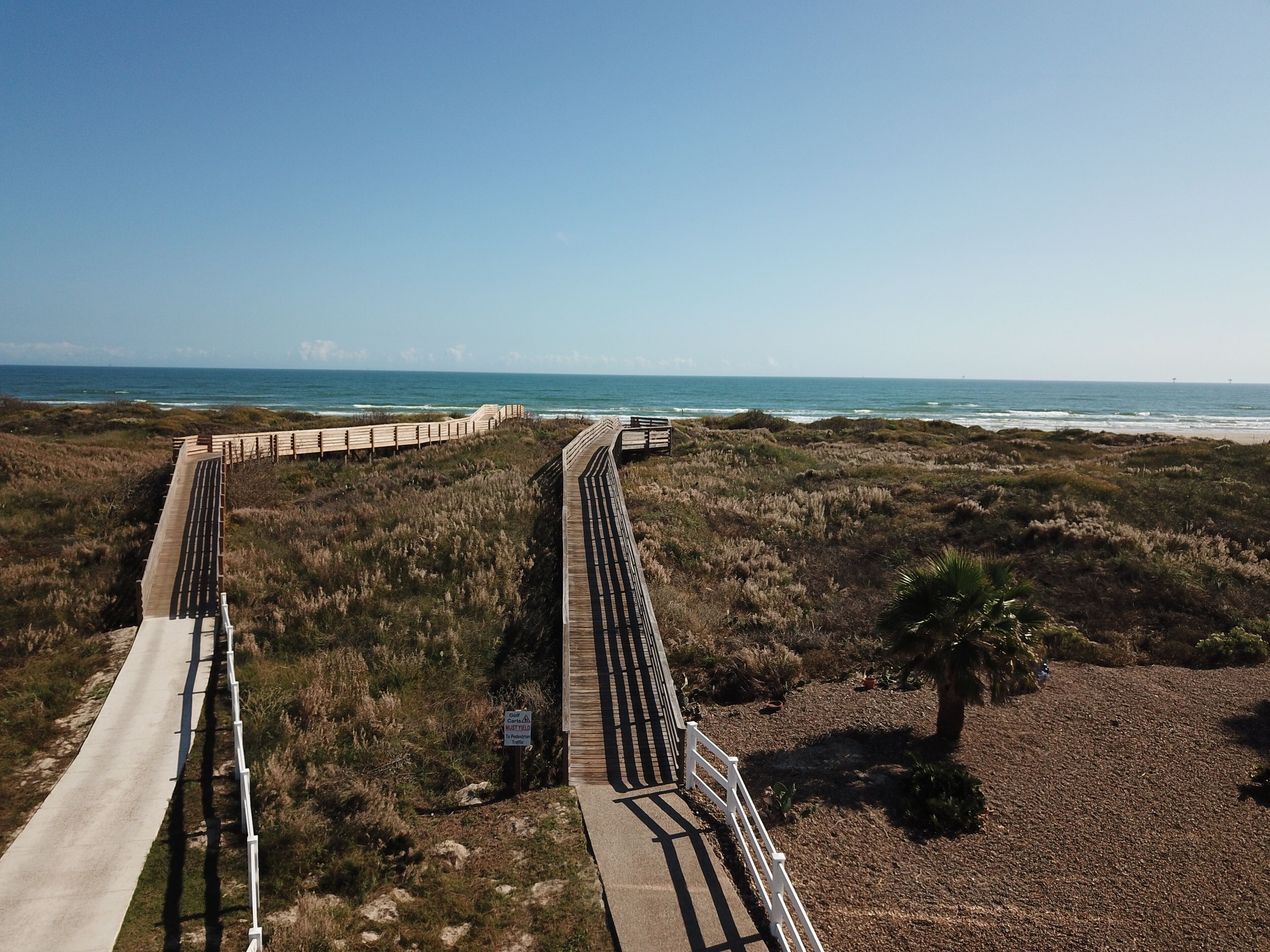 A coastal boardwalk with a clear view of the ocean and beach.
