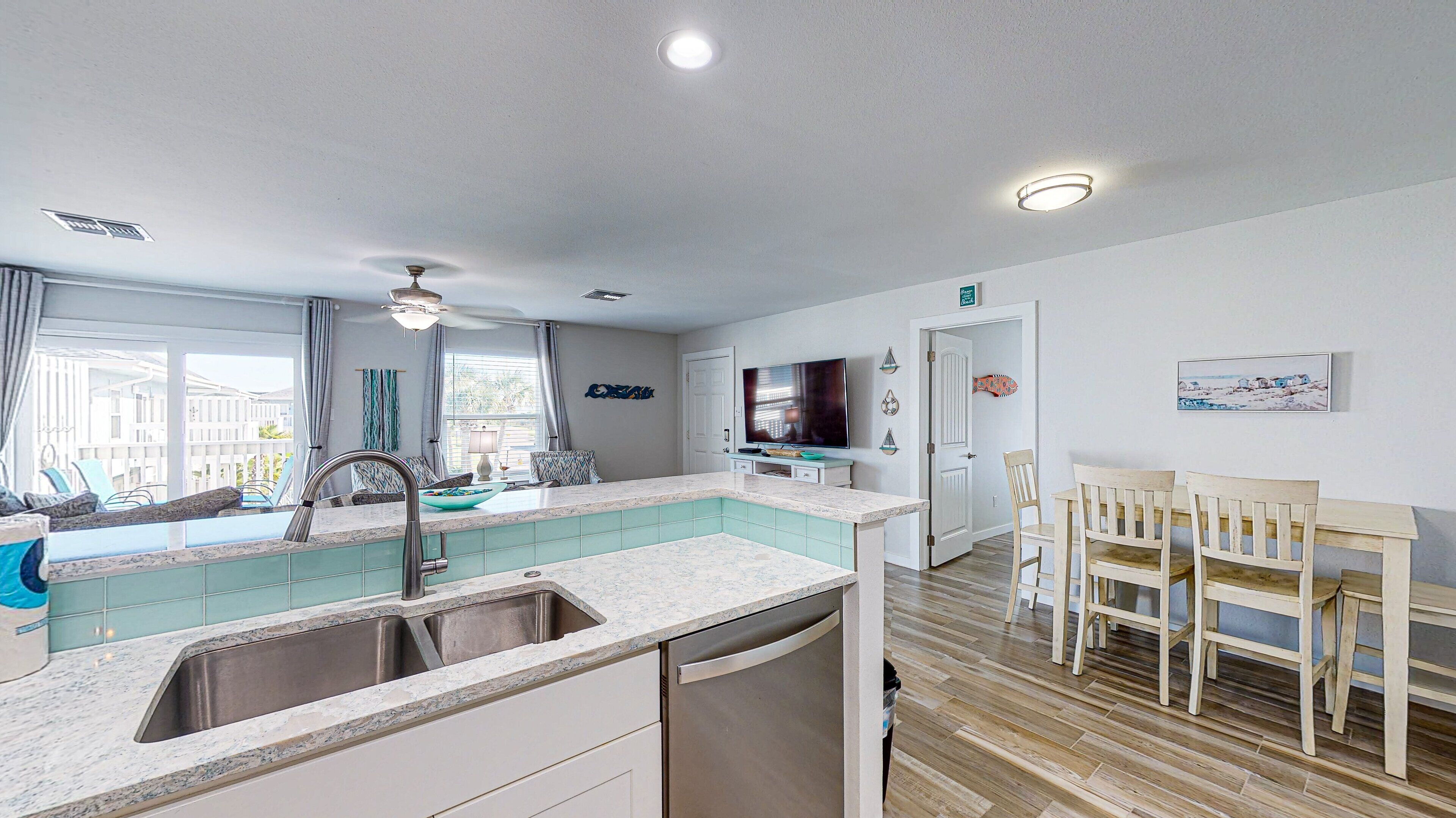 A modern kitchen with a built-in dishwasher, a dining area with wooden chairs, and a view of the outside balcony.