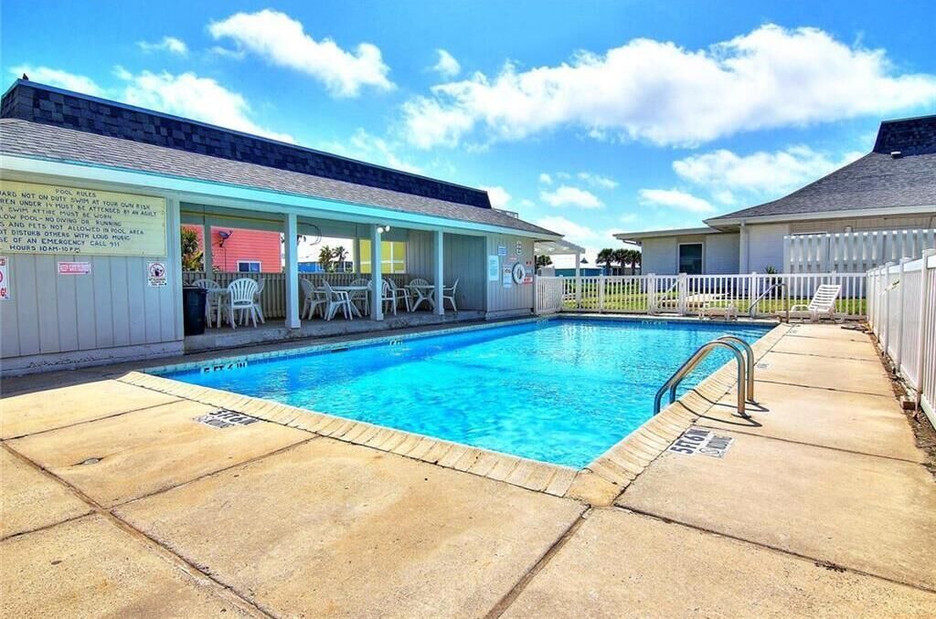 Una piscina con una zona de estar techada y un deck con valla.