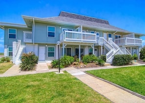 A two-story building with a balcony on the second floor, a covered porch, and a staircase leading to the upper level. - Second Floor Condo, Shared Pool, Grills and Boardwalk (Port Aransas)