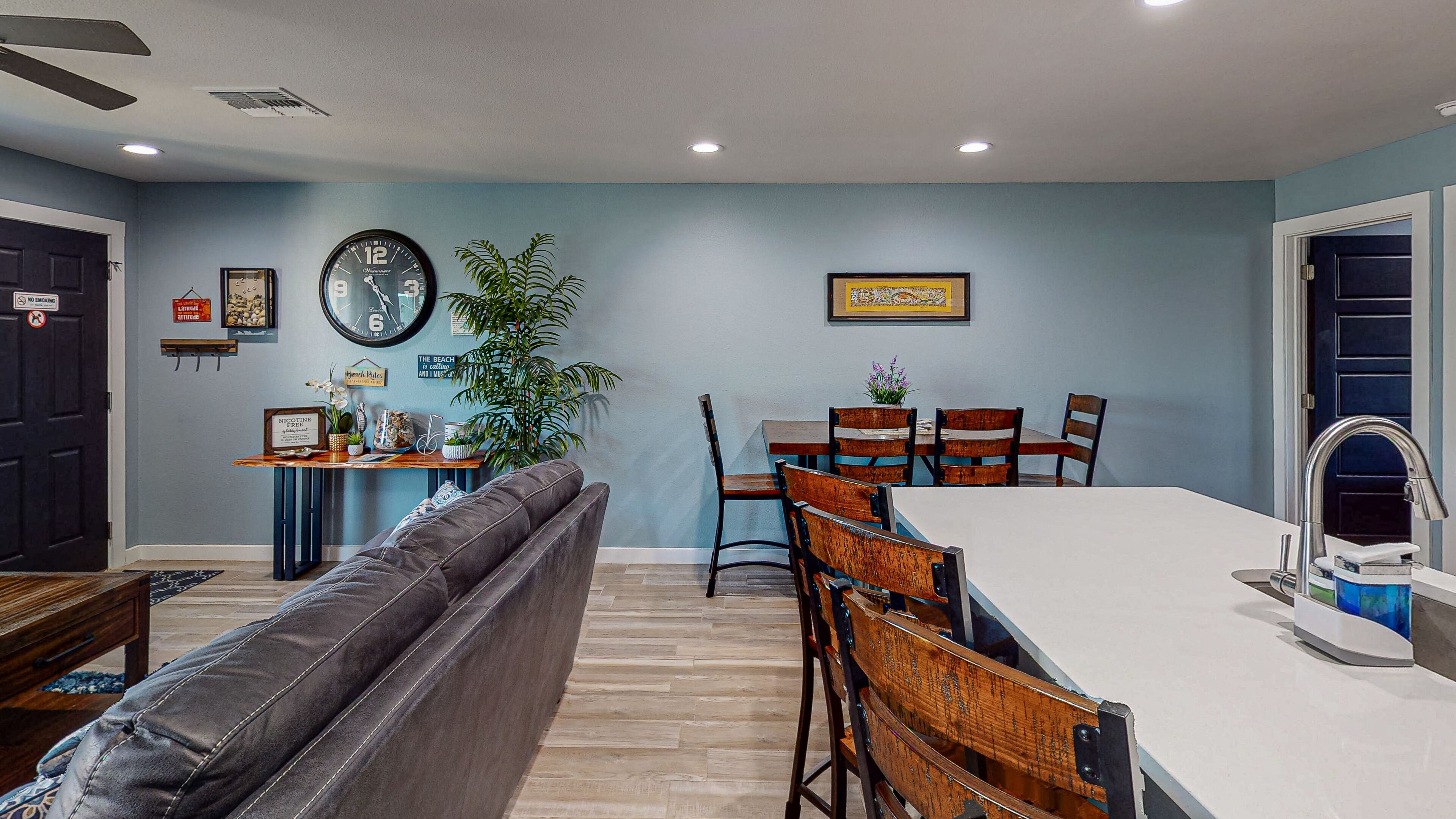 A dining area with a table and chairs, a clock on the wall, and a plant.