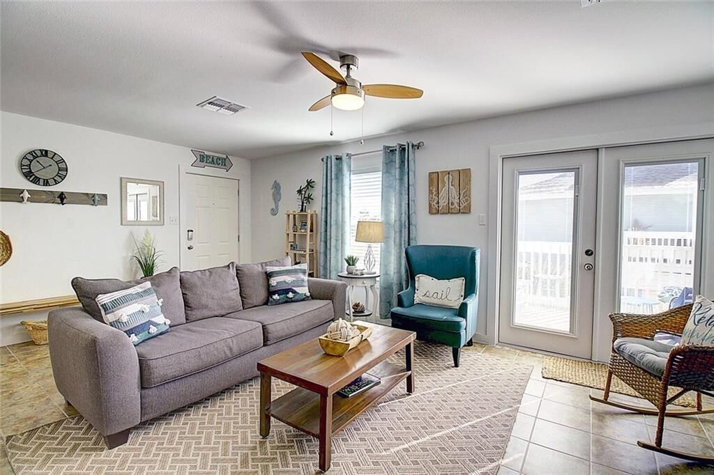 A living room with a gray sofa, a wooden coffee table, a teal armchair, and a wicker rocking chair.