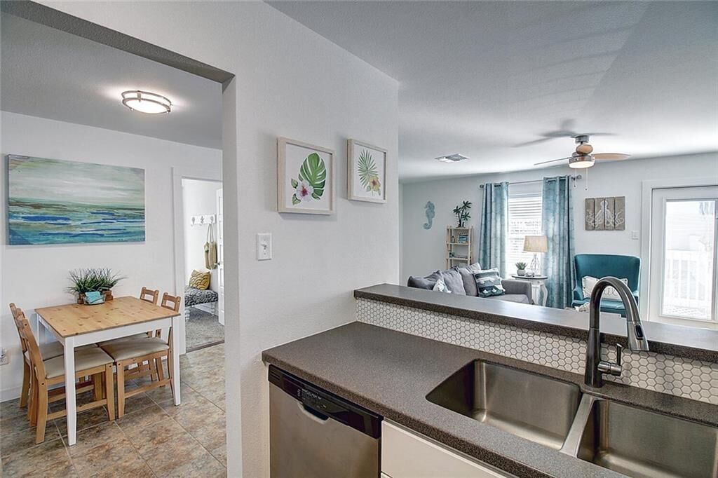 A modern kitchen with a dishwasher, a sink, and a dining area with a wooden table and chairs.
