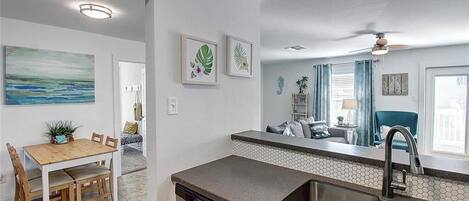 A modern kitchen with a dishwasher, a sink, and a dining area with a wooden table and chairs.