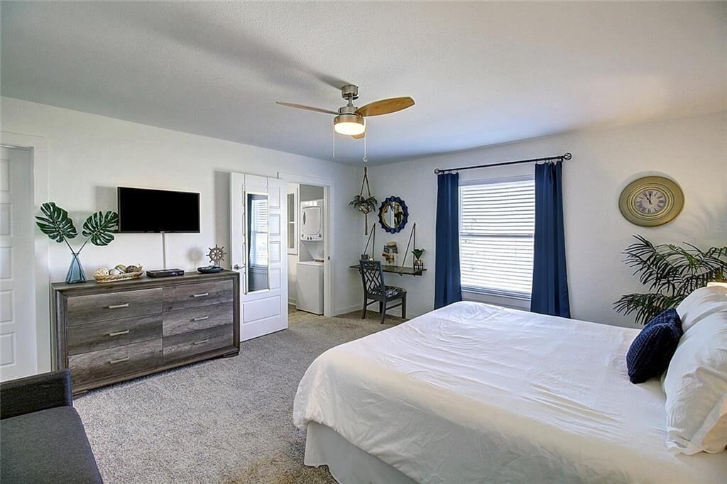 A bedroom with a bed, a ceiling fan, a TV, a dresser, a desk, and a window with curtains.