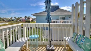 A wooden deck with a white fence, a blue umbrella, a round table, and a cushioned bench with patterned cushions. - Pet Friendly, Second Floor Condo, Shared Pool and Grill, Boardwalk (Port Aransas)