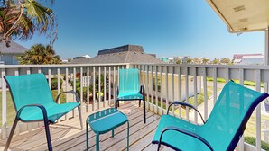 A wooden deck with turquoise chairs and a view of a pyramid-like structure in the distance. - Second Floor Condo, Pet Friendly, Shared Pool and Grill, Boardwalk (Port Aransas)