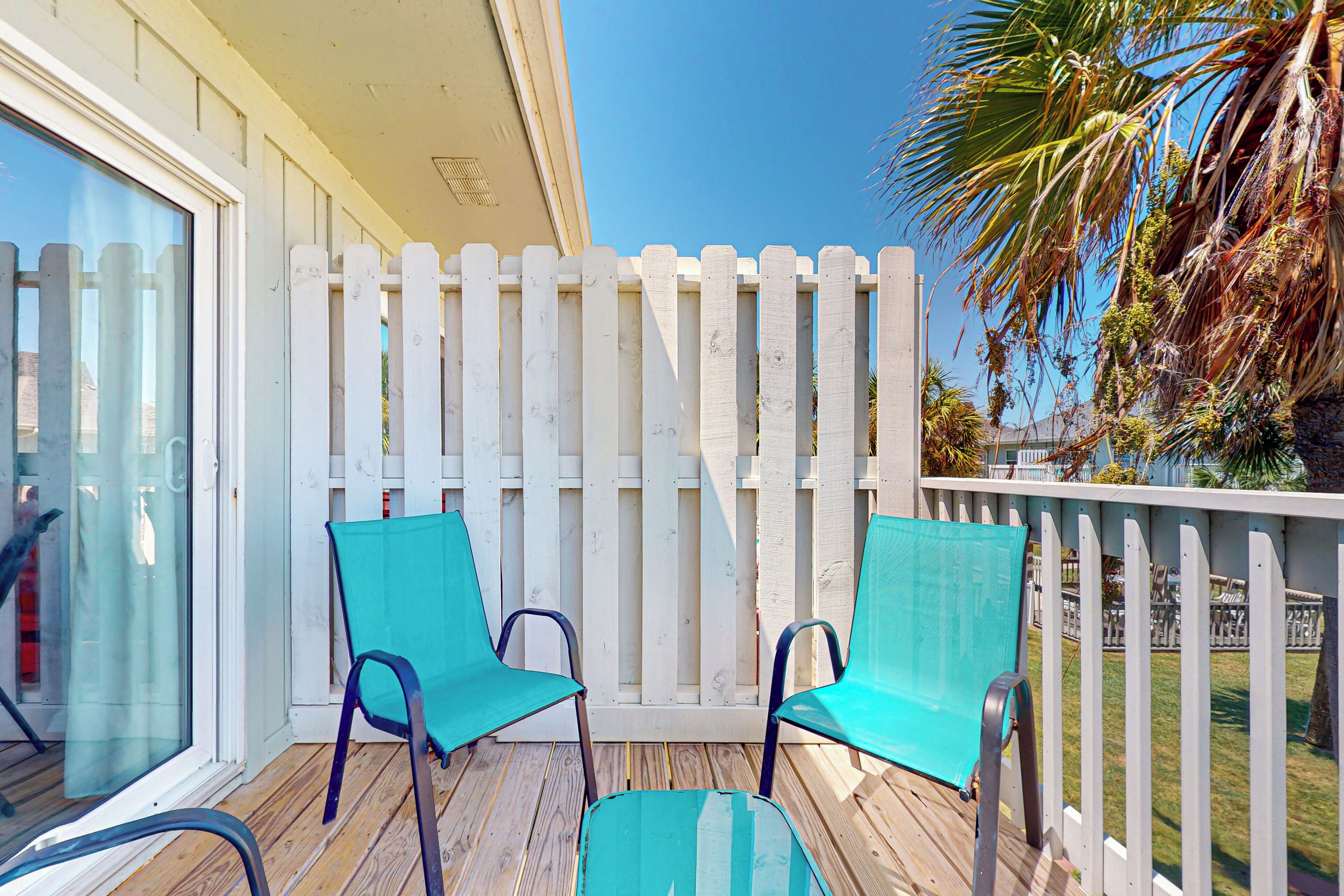 Une terrasse en bois avec deux chaises turquoise et une porte vitrée.