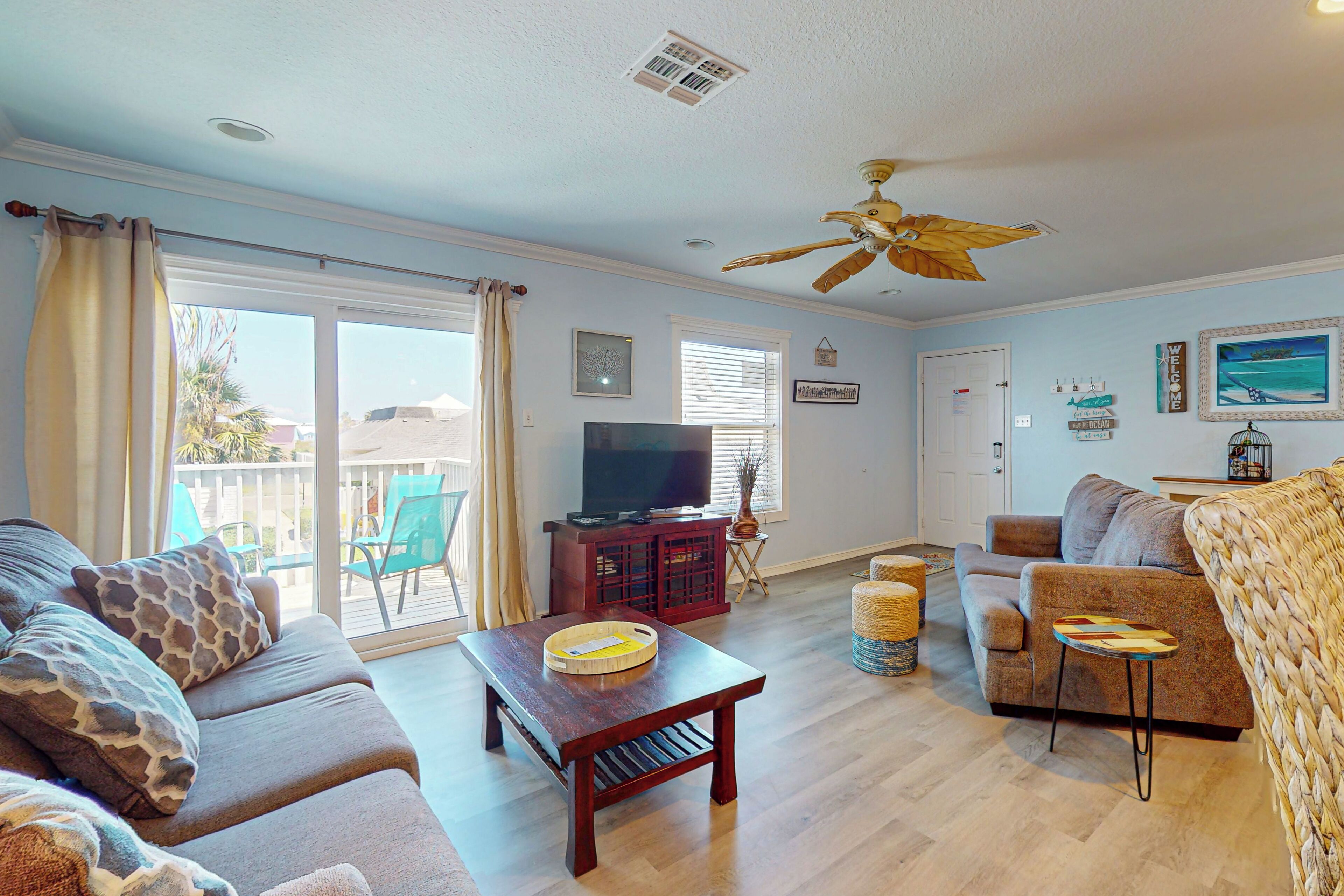 A spacious living room with a sofa, a coffee table, a TV on a stand, and a ceiling fan.