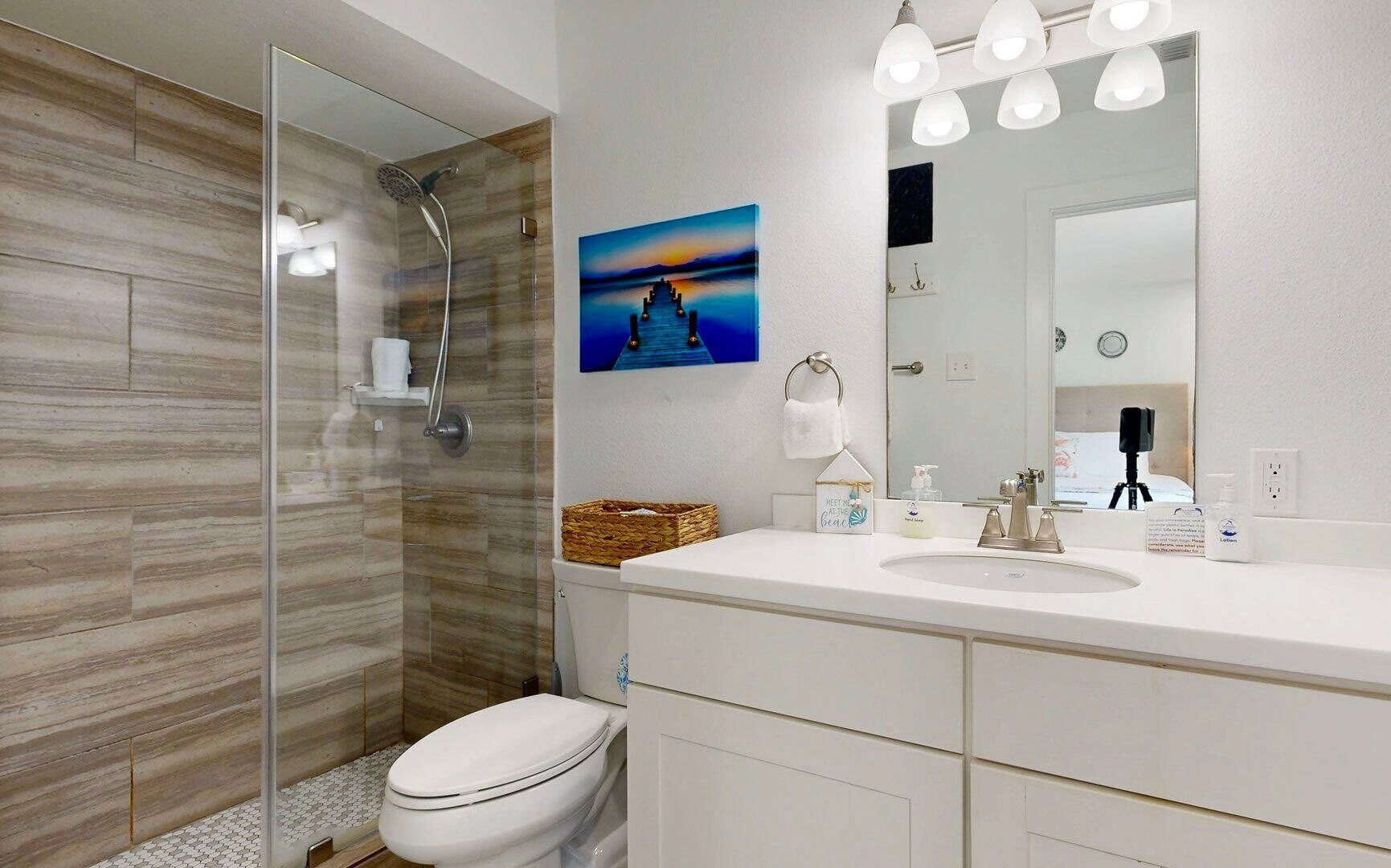Un bagno moderno con box doccia in vetro, lavandino bianco e un ampio specchio illuminato.