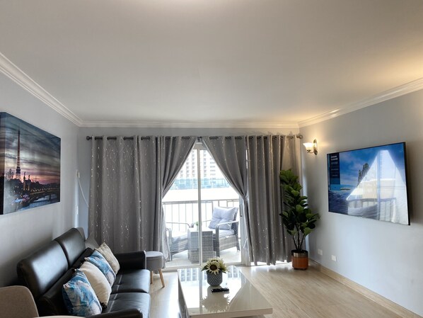 Een moderne woonkamer met een bank, salontafel en grote ramen met gordijnen.