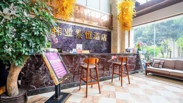 A reception area with a marble counter, two wooden chairs, a sofa, and a potted tree.