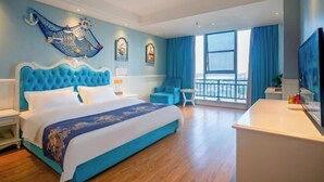 Habitación de hotel con una cama grande, un escritorio, una silla, un balcón con vistas y obras de arte en las paredes.