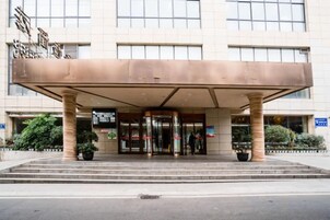 Entrada de hotel con acceso cubierto, un juego de puertas dobles y un pequeño jardín con plantas en macetas.