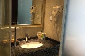 Un baño con lavamanos de mármol, cabina de ducha de vidrio y dos secadores de pelo montados en la pared.