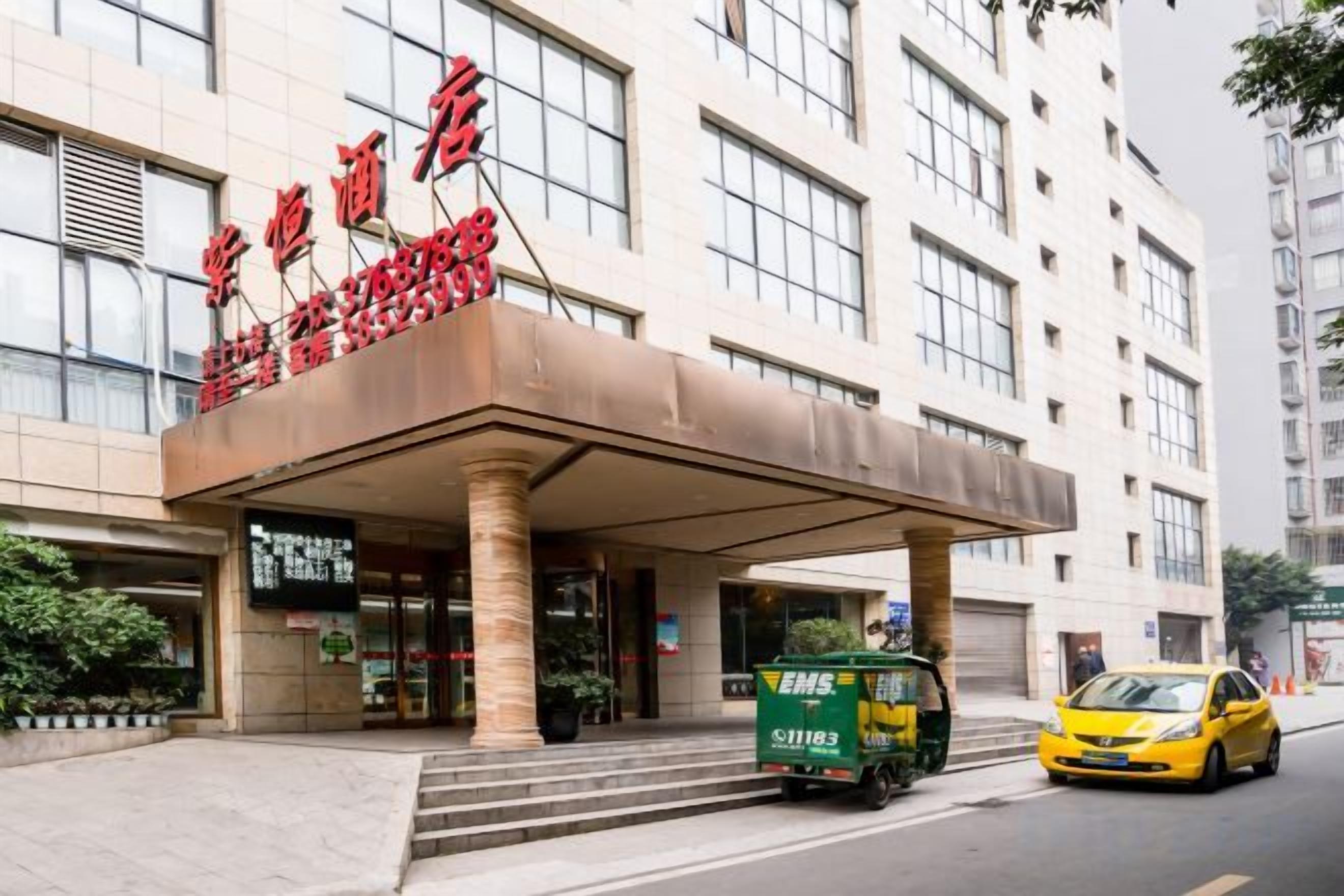 Entrada de hotel con vestíbulo techado, un taxi y un camión de reparto.