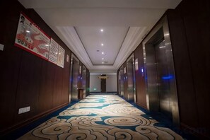A hotel hallway with a patterned carpet, wooden walls, and a ceiling with recessed lighting. - Ziheng Hotel (Meishan)