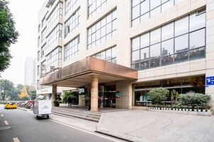 Une entrée d’hôtel moderne, dotée d’une allée couverte, d’un espace de stationnement et offrant une vue dégagée sur la rue.