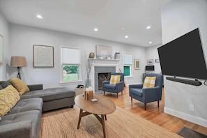 A modern living room with a fireplace, sofas, armchairs, and a TV mounted on the wall.