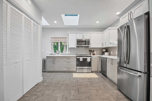 A modern kitchen with white cabinets, stainless steel appliances, and a herringbone floor pattern.