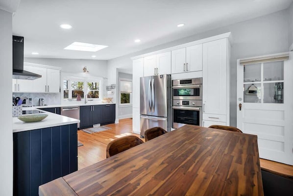 Una cocina moderna con armarios blancos, electrodomésticos de acero inoxidable y una mesa de comedor de madera.