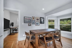 Un comedor con una mesa y sillas de madera, una cocina con encimera negra y cuadros en la pared.