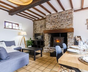 Una sala de estar acogedora con chimenea de piedra, un sofá, un televisor y un comedor listo para una comida.