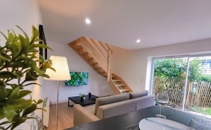 A modern living room with a staircase, a TV, and a dining area with a table and chairs. - "La Boétie II" - 50 m2 de Charme Limoges Centre (Limoges)