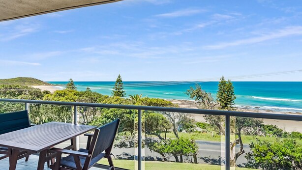 Ein Balkon mit Tisch und Stühlen mit Blick auf einen Strand und den Ozean.