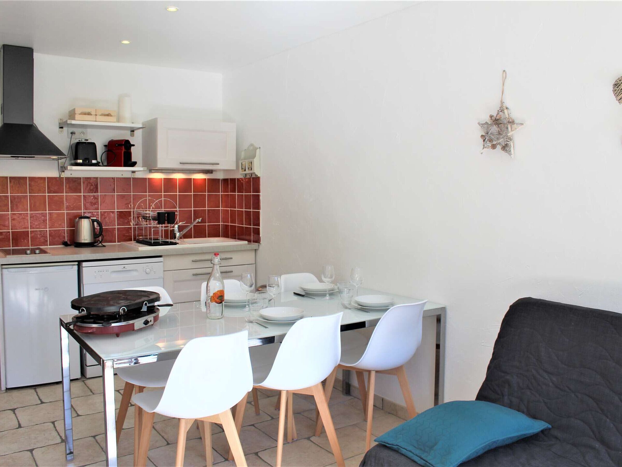 Una cocina compacta con comedor, sillas blancas y un sofá con un cojín azul.