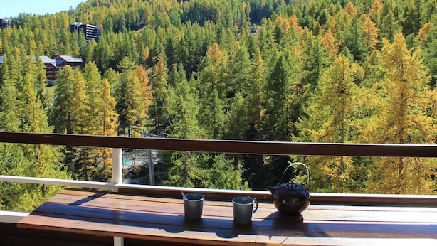A balcony with a wooden railing, a metal teapot, and two metal cups.