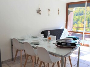 A dining area with a glass table, white chairs, and a view of a forest through a large window.