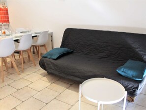 A living area with a dark grey sofa, two teal cushions, a white round table, and a dining setup with white chairs and a white table.