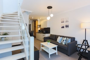 Un salon moderne avec un escalier, un canapé, une table basse et une cuisine en arrière-plan.
