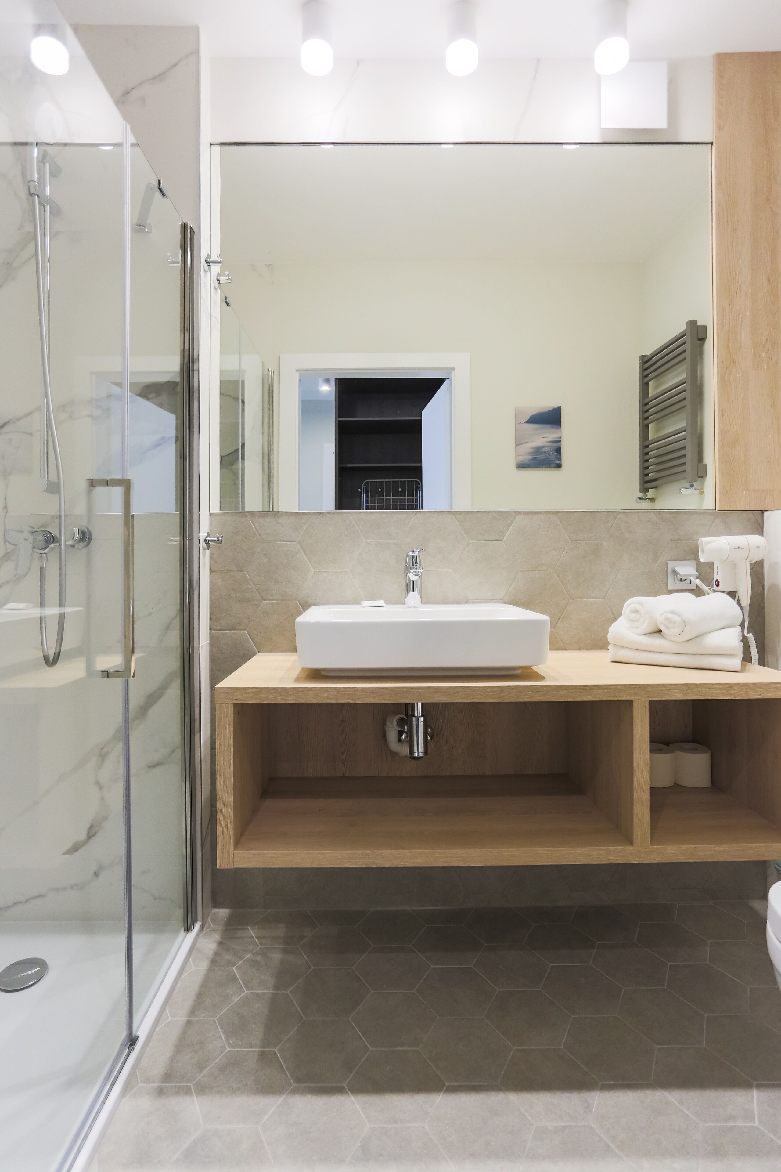 Un bagno moderno con cabina doccia in vetro, lavandino bianco e mobile contenitore in legno.