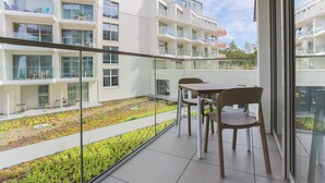 Un moderno edificio residenziale con un balcone che offre un tavolo e sedie, una ringhiera in vetro e vista su un giardino curato.