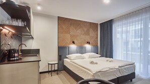 Una camera d'albergo moderna con un letto, un comodino e un angolo cottura integrato con macchina del caffè.