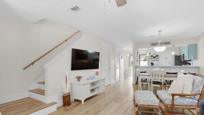 Ein modernes Wohnzimmer mit Treppe, Flachbildfernseher, Essbereich und Küche.