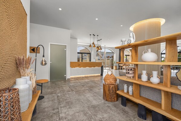 Un interior moderno con un mostrador de recepción, estanterías de madera con objetos decorativos y un gran tapiz tejido.