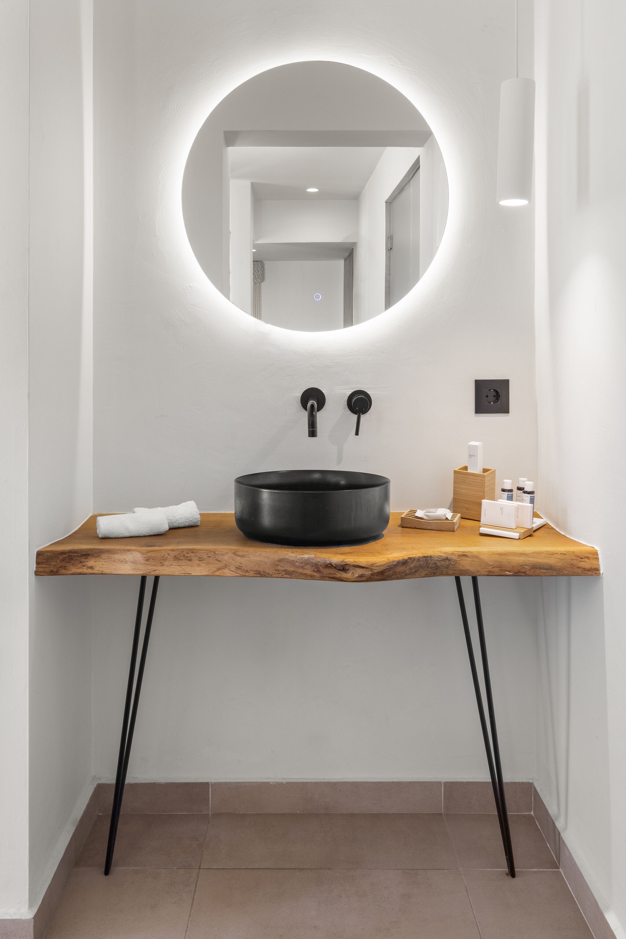 A modern bathroom with a round mirror, black sink, wooden vanity, and a towel on the counter.