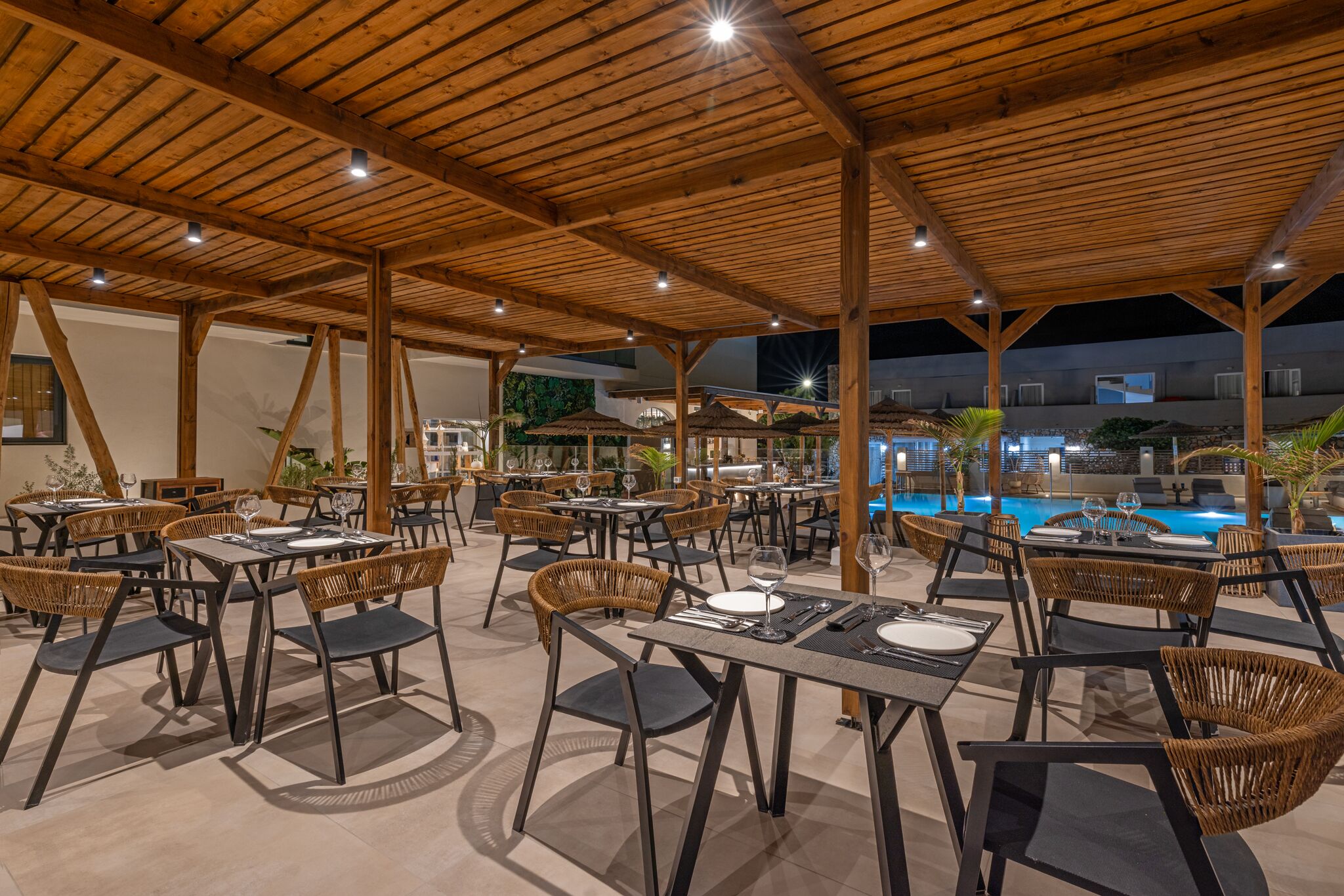 Un espace extérieur aménagé pour les repas, avec des tables et des chaises, une piscine et une structure de plafond en bois.