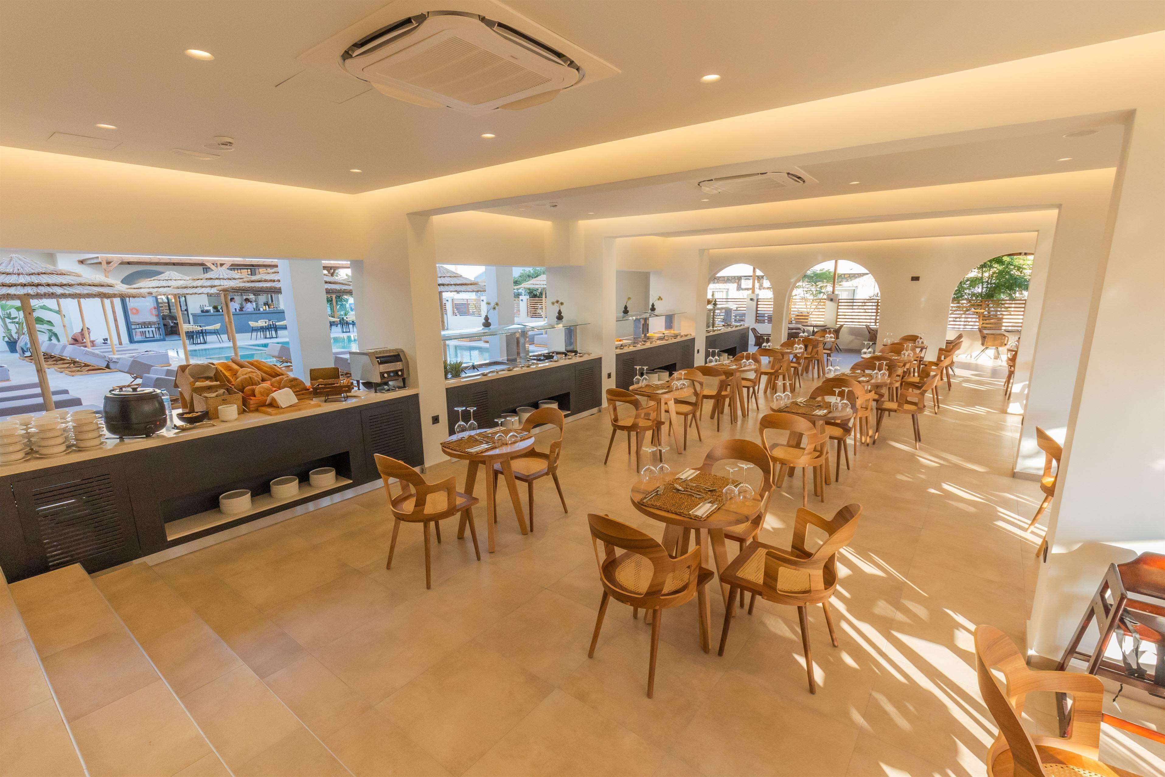 A spacious dining area with multiple tables and chairs, a buffet counter, and large windows allowing natural light.
