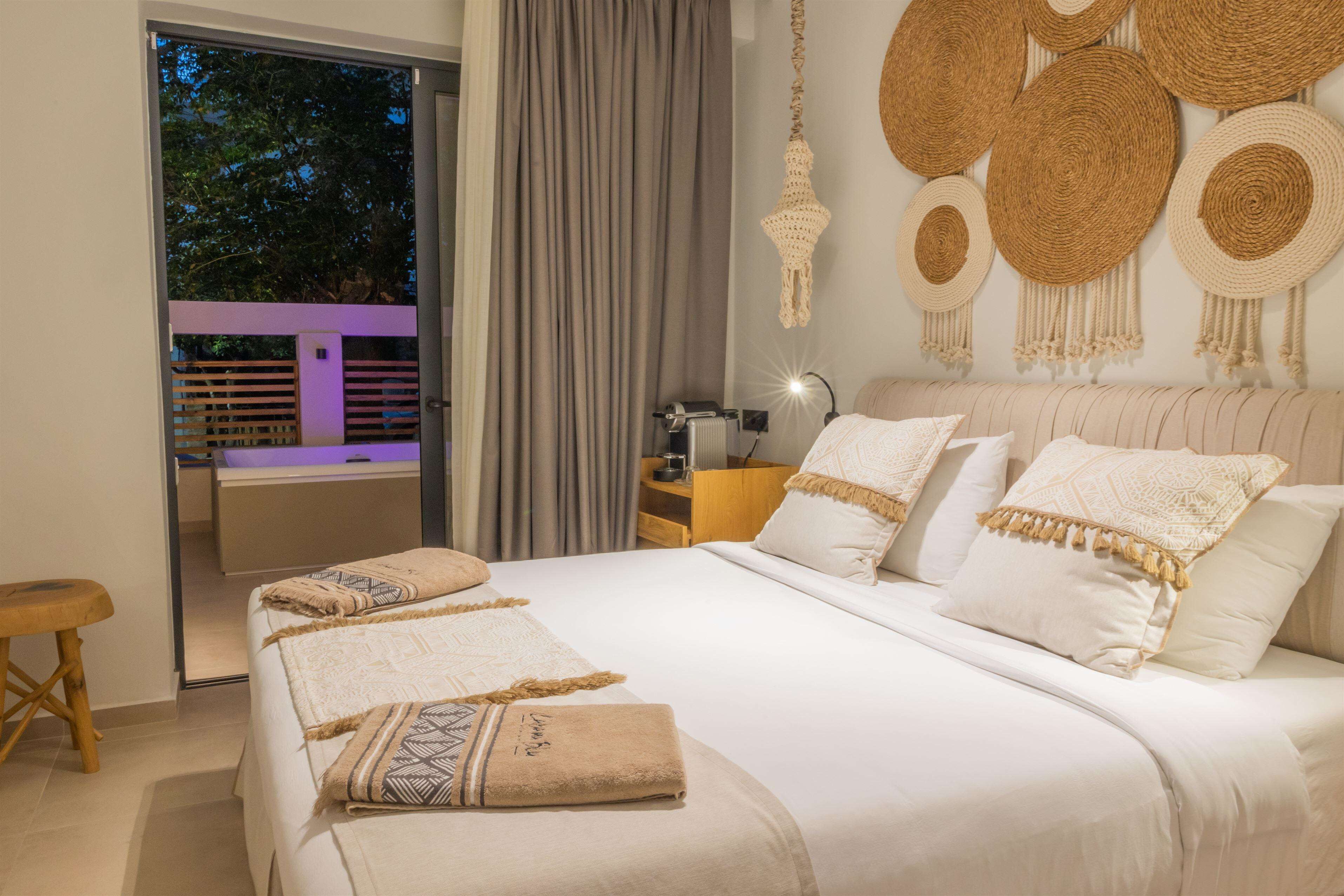 A bedroom with a large bed, a nightstand, a lamp, and a view of the outdoors.