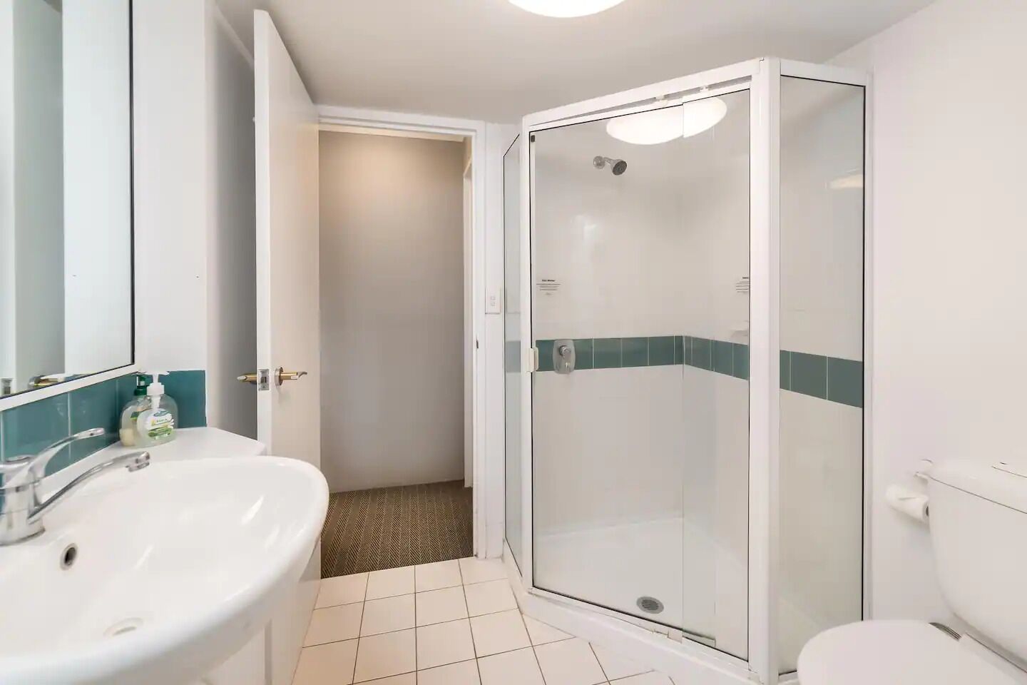 A bathroom with a white sink, a mirror, a glass-enclosed shower, and a toilet.